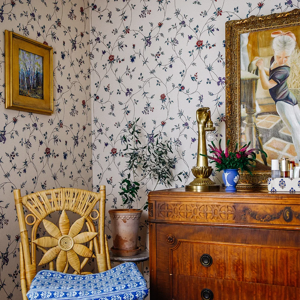 Guest bedroom with tan chintz vine wallpaper and a dresser, chair and art.