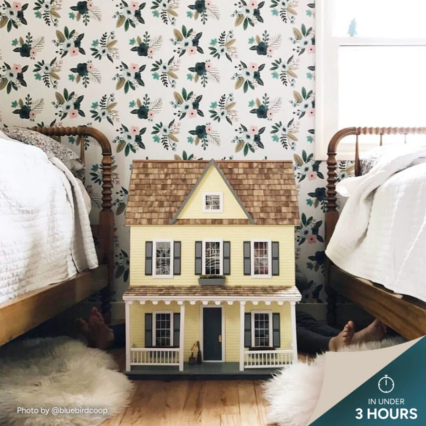 Dollhouse between two beds with floral wallpaper.