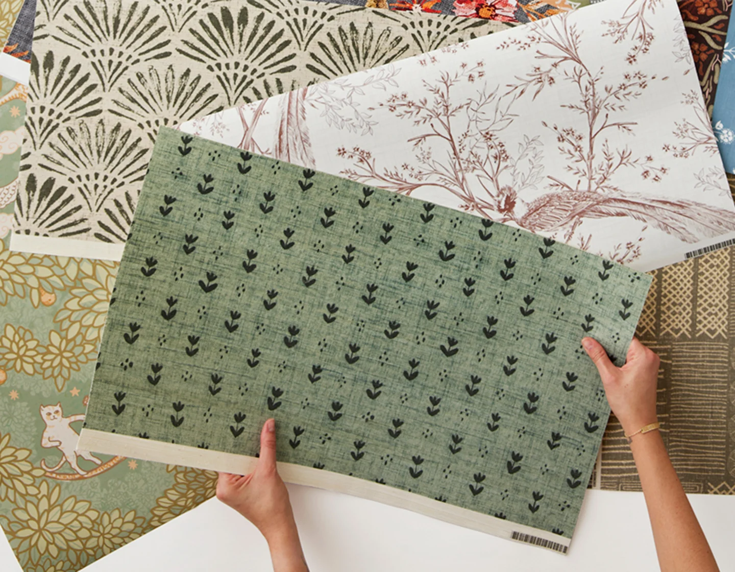 Hands holding a green wallpaper swatch.