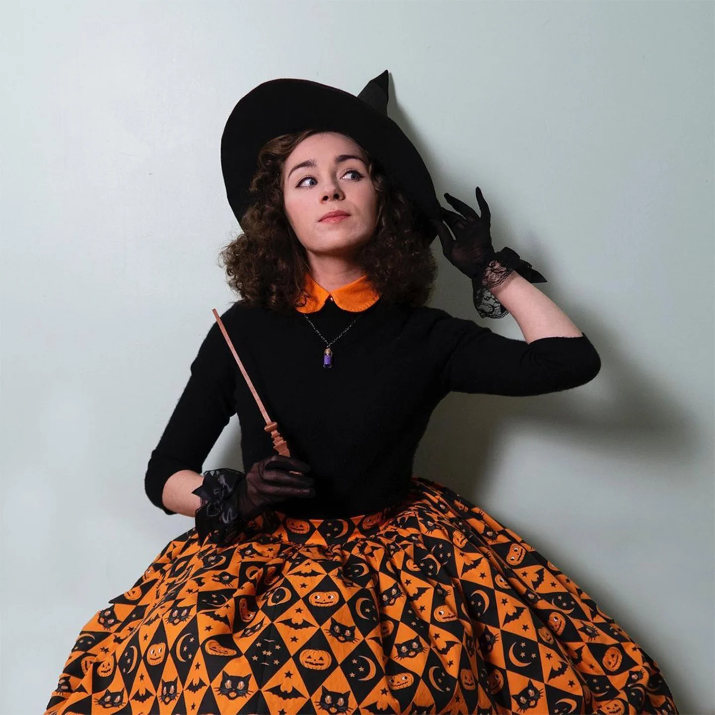 Girl in witch hat with black top and poofy black and orange halloween patterned skirt.